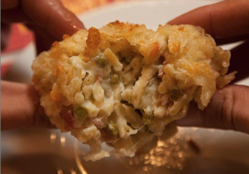 A close-up of a hand holding a piece of food with a golden-brown crust, possibly a baked dish with visible green specks. 3