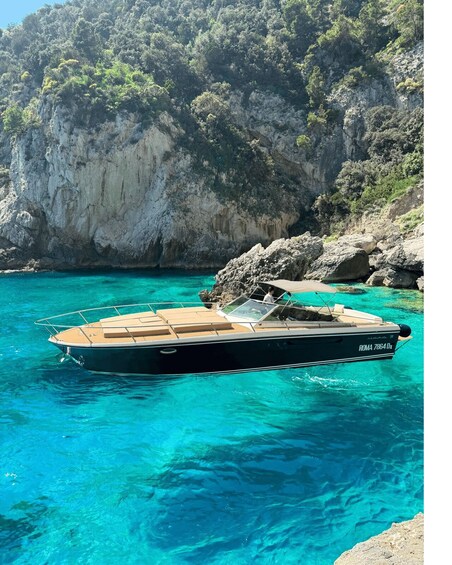 A boat named 'ROMA 7864 Dx' anchored near a rocky coastline with clear turquoise water. 1