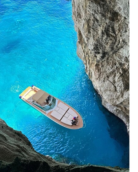 A boat with a covered deck and lounge chairs anchored near a rocky coastline. 4
