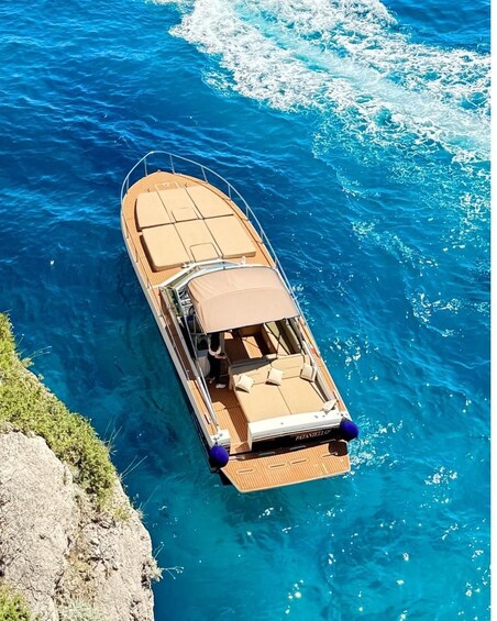 A boat with a wooden deck and a canopy, anchored near a rocky coastline. 3