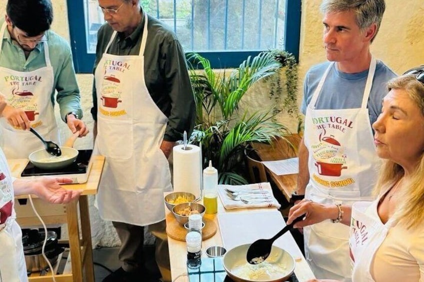 A cooking class with participants wearing aprons, cooking on a stove. 1