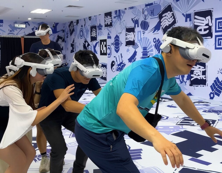 People wearing VR headsets in a room with a patterned wall. 3