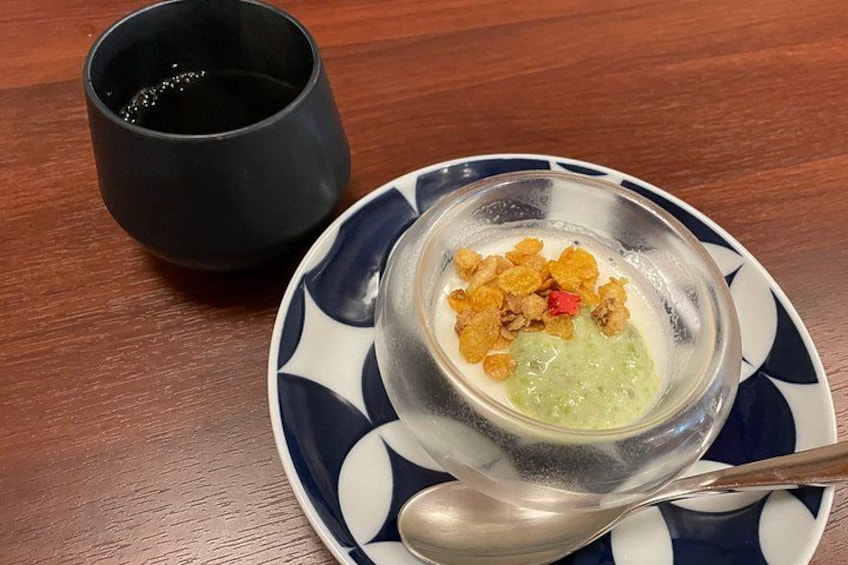 Eine Schüssel Suppe mit Cornflakes auf einem Teller, ein Löffel und eine schwarze Tasse auf einem Holztisch. 2