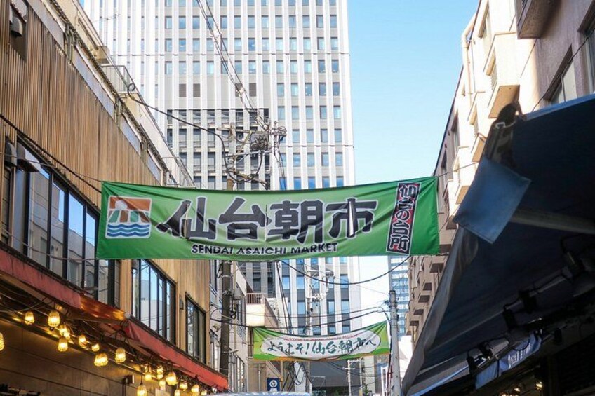 Straßenszene mit einem grünen Banner, das den Sendai Asai Markt bewirbt. 3