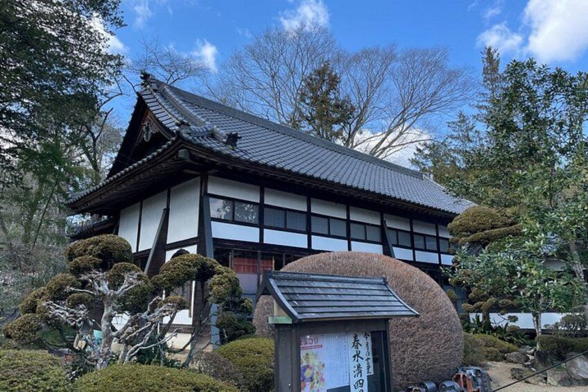 A traditional Japanese building with a tiled roof, surrounded by well-maintained bushes and trees. 2