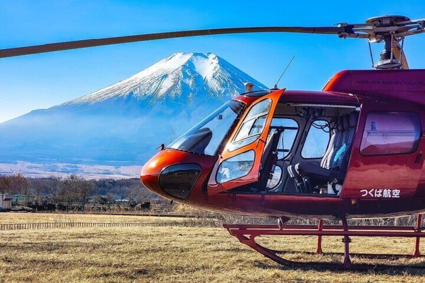 Un elicottero rosso con lo sportello aperto, parcheggiato in un campo con una montagna innevata sullo sfondo. 2