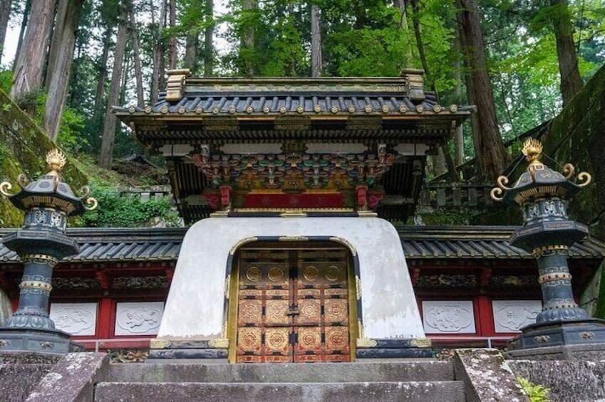 A traditional temple with a large wooden door, ornate decorations, and a forested backdrop. 1
