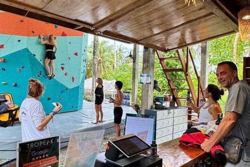 Eine Kletterwand, eine Person beim Klettern sowie ein Tisch mit Kletterausrüstung und einem Laptop. 4