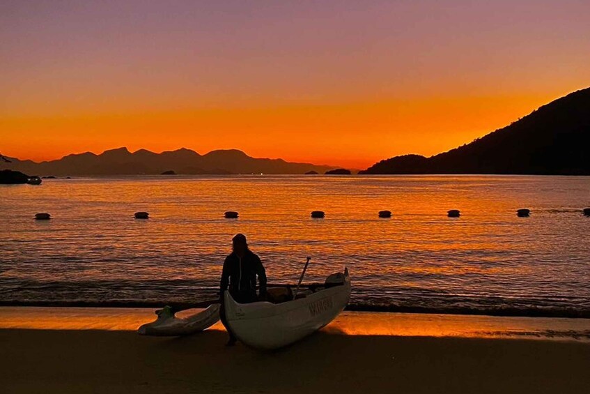 A person in a boat on a beach at sunset with mountains in the background. 1