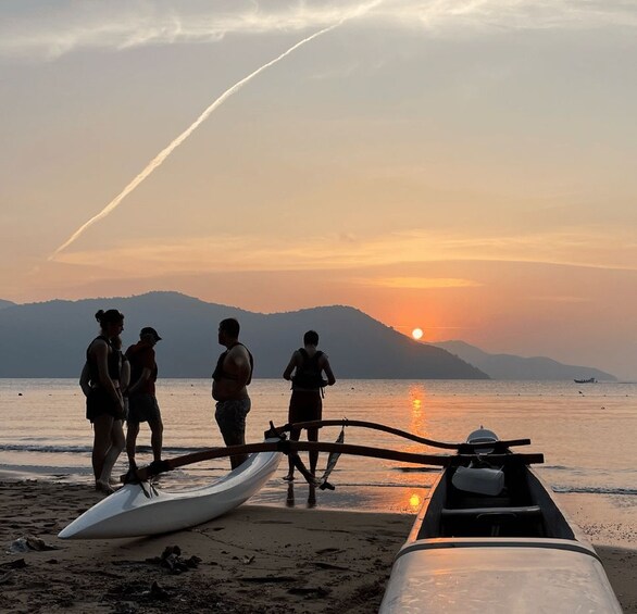 A sunset over a beach with people standing near boats. 3