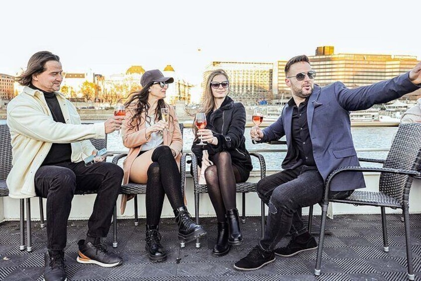 Cuatro personas en un bote, sosteniendo copas de vino, con un paisaje urbano al fondo. 1