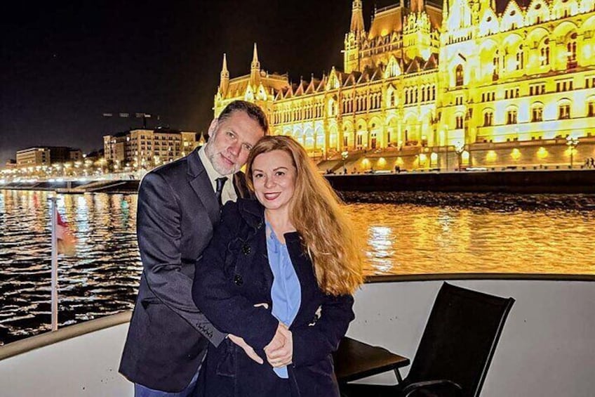 Una pareja en un barco con un edificio histórico iluminado al fondo. 4