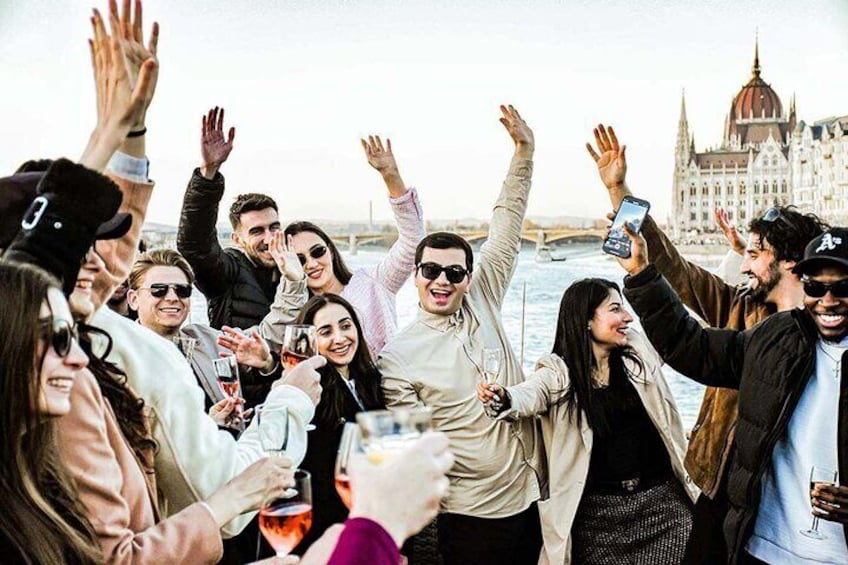 Un grupo de personas celebrando con bebidas, un río y un edificio histórico al fondo. 5