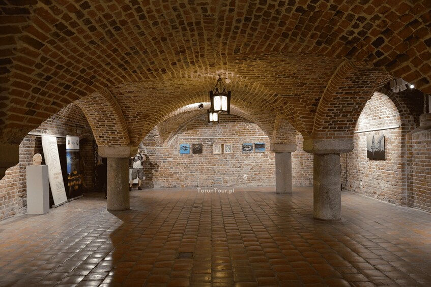 An arched brick ceiling, stone columns, and a tiled floor in a historical building. 2