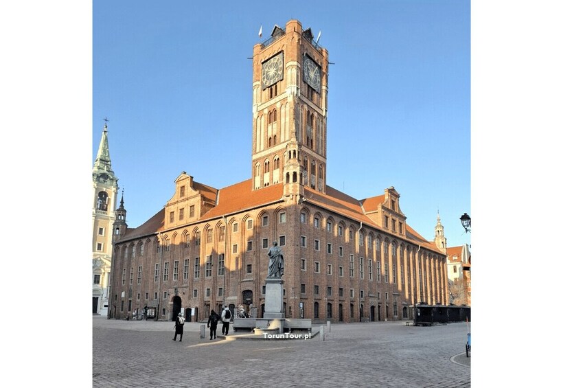 A historic building with a prominent clock tower, a statue in front, and a clear blue sky. 1