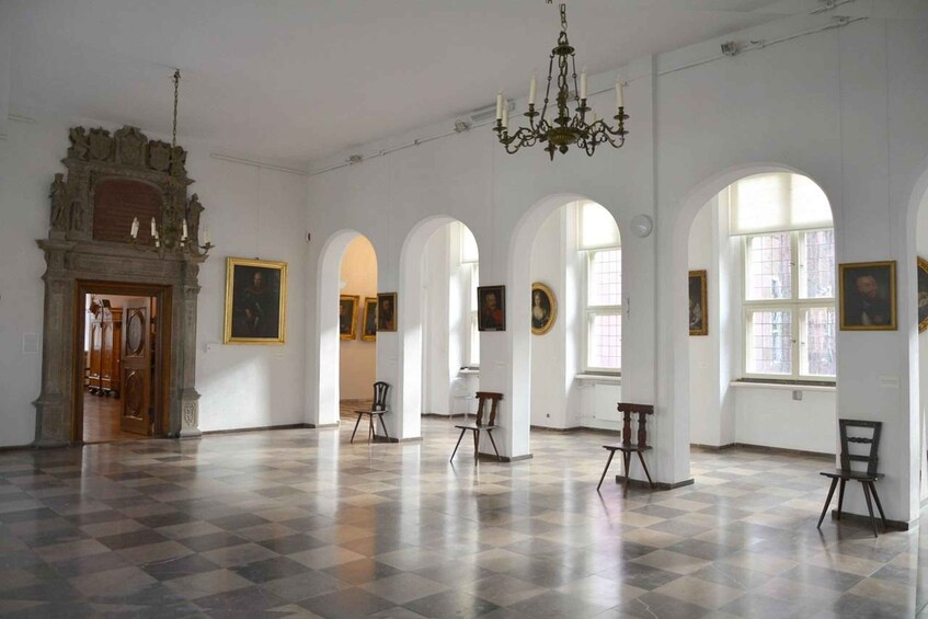 A spacious room with a checkered floor, arched windows, and a chandelier. 4