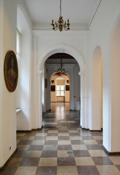 A hallway with checkered flooring, white walls, and a chandelier. 5