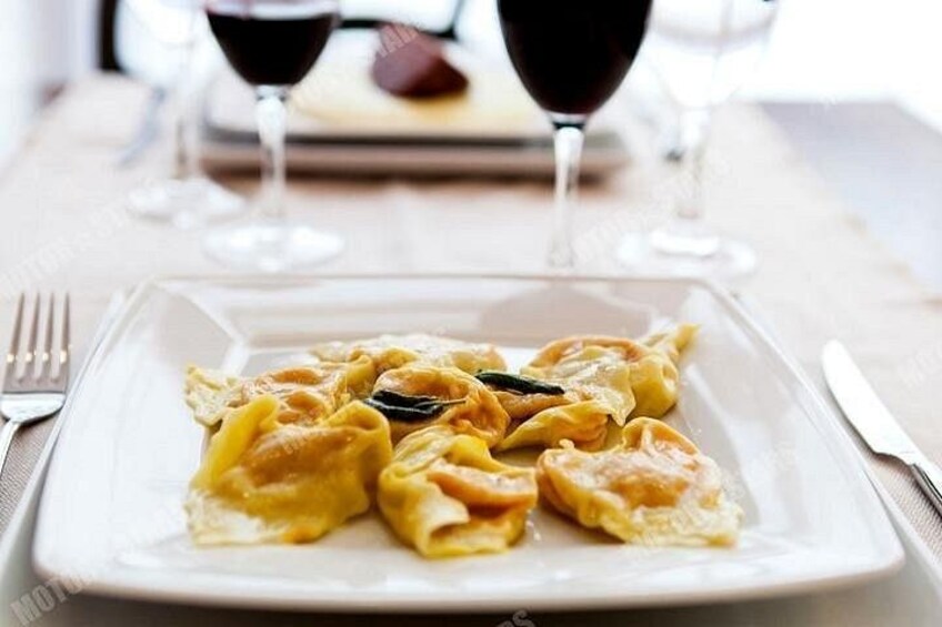 A plate of ravioli with a fork and knife on the side, and two glasses of red wine in the background. 4