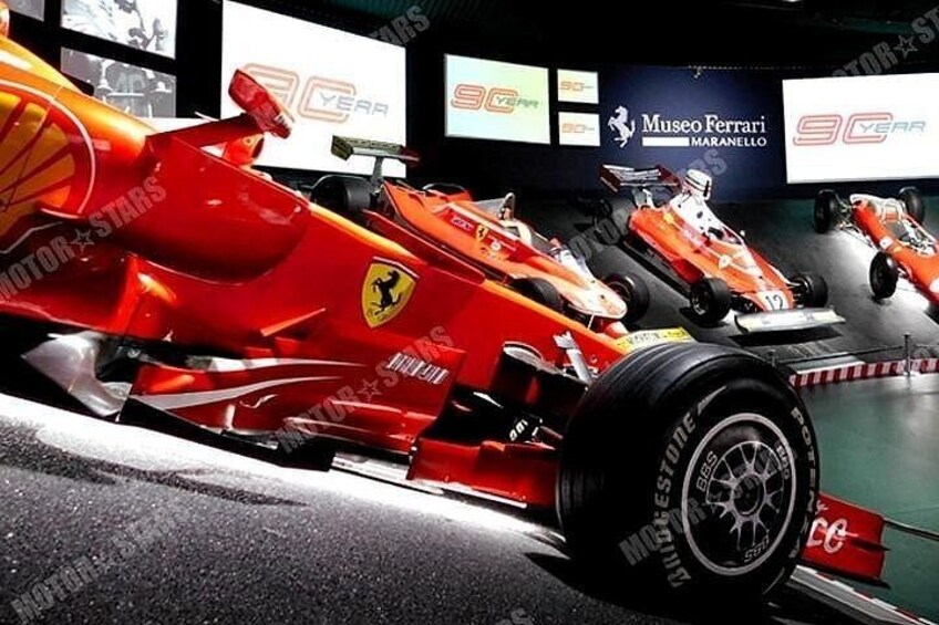 A red Ferrari race car in a museum setting with other cars and advertisements. 5