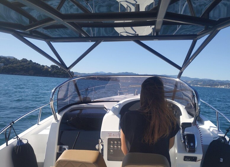 A boat with a woman seated at the helm, navigating through calm waters with a coastline in the distance. 4