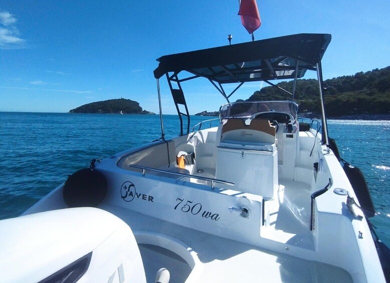 A boat named '750 Owa' with a canopy, on a calm sea with a hilly island in the background. 3
