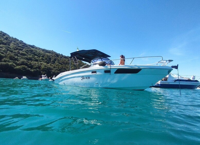 A white boat named 'JAVER' on turquoise water with a forested hill in the background. 2