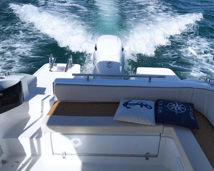 A boat's interior with a cushioned seating area, a steering wheel, and a wake behind the vessel. 1