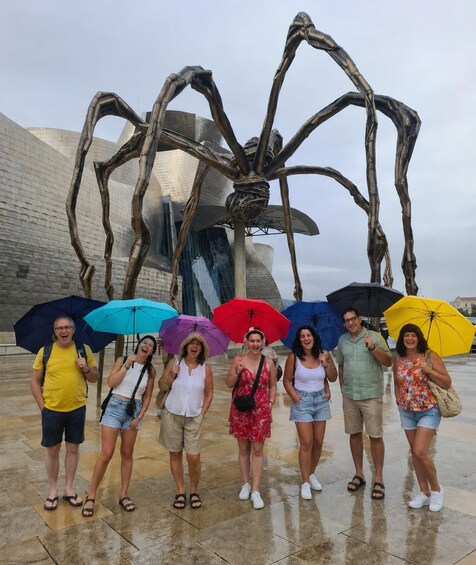 A group of people standing in front of a large metallic sculpture resembling a giant spider. 4