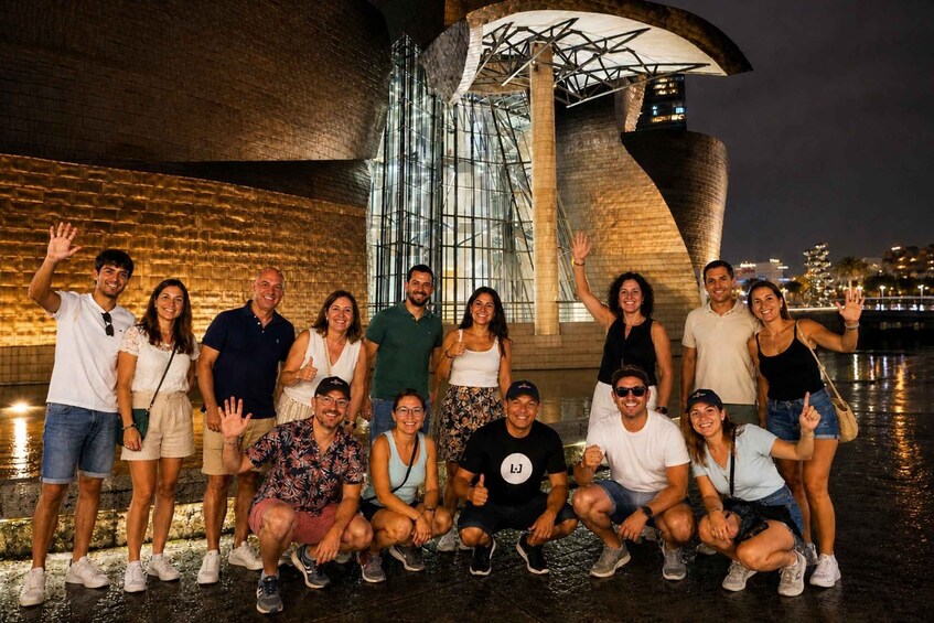 A group of people posing in front of a modern architectural structure with a reflective surface and a unique curved design. 2