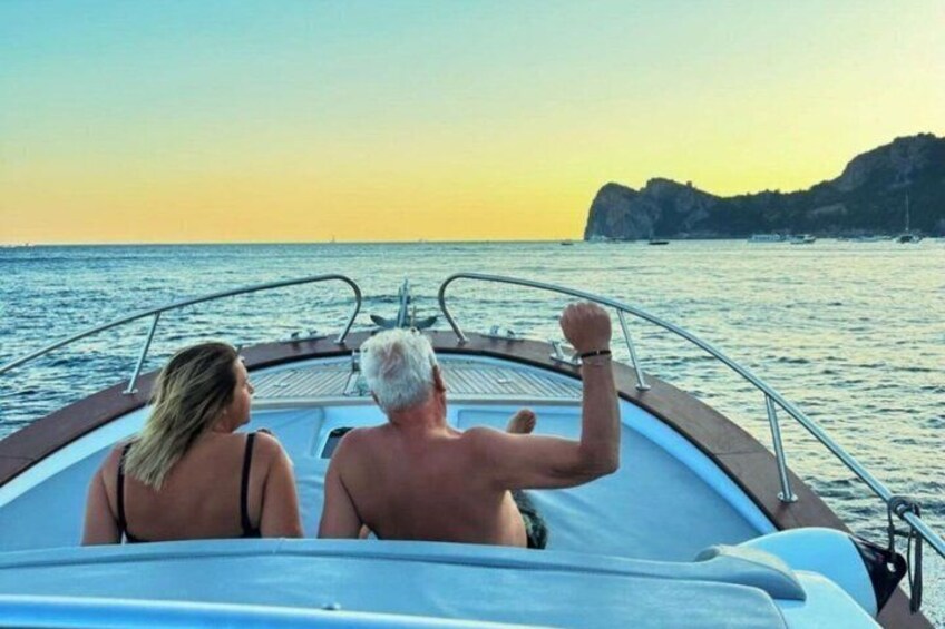 A boat with two people on the deck, a calm sea, and a sunset in the background. 3