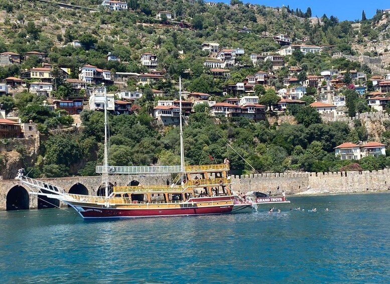 A boat named 'Grand Tories' docked near a hillside with houses. 1