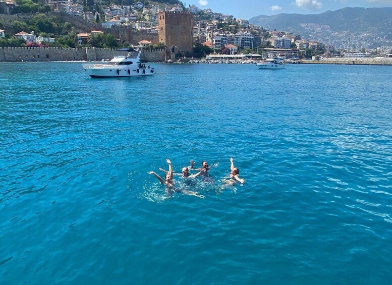 A group of people swimming in a clear blue sea with boats and a historic castle in the background. 4
