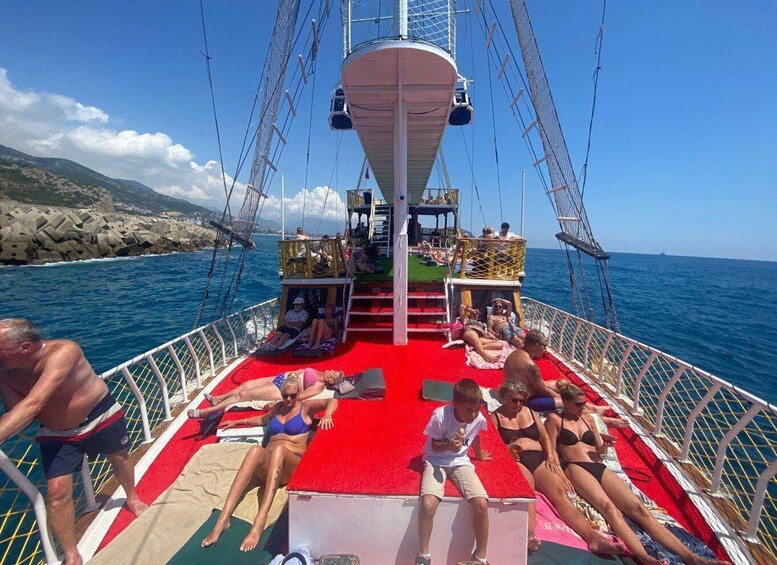A boat deck with people sunbathing, a red carpet, and a rocky coastline in the background. 5