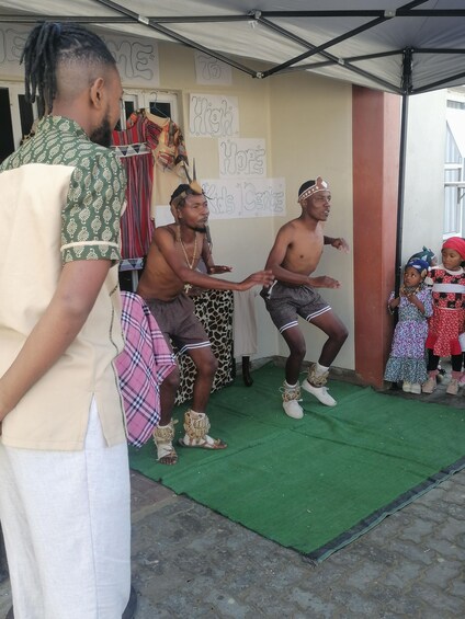 A group of people performing a dance in a covered outdoor area with a green floor. 3