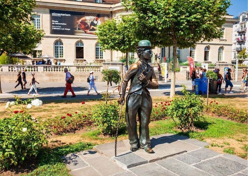 A statue of a man with a cane in a public square with buildings and pedestrians in the background. 5