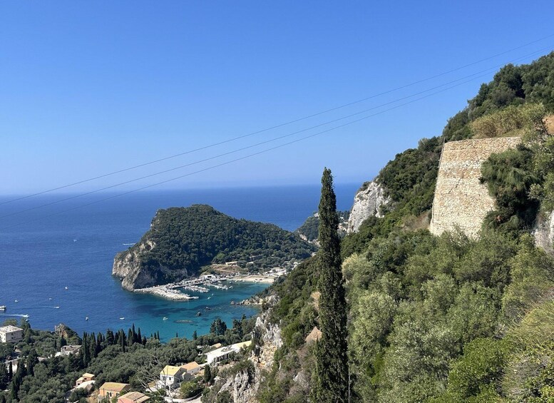 A coastal landscape with a rocky cliff, a small island with dense vegetation, and a marina with boats. 5
