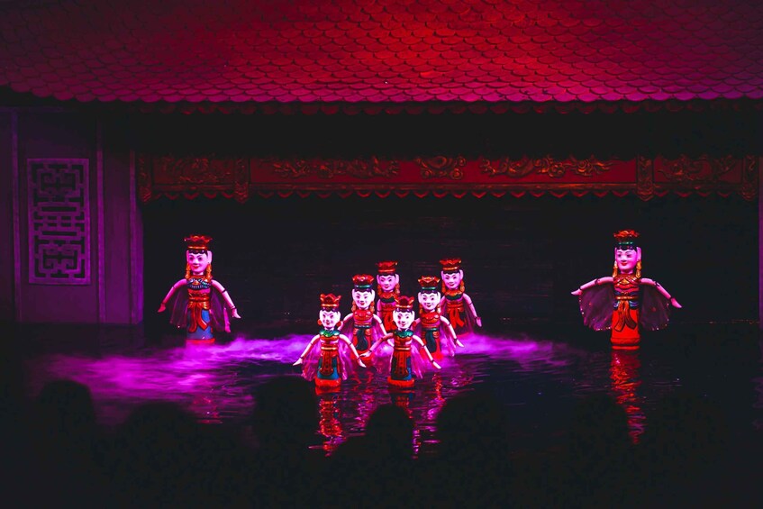 A stage with performers in traditional costumes, a tiled roof, and a decorative wall. 1