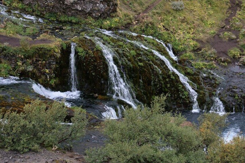 Ein Wasserfall stürzt über moosbewachsene Steine herab, umgeben von dichtem Grün. 5