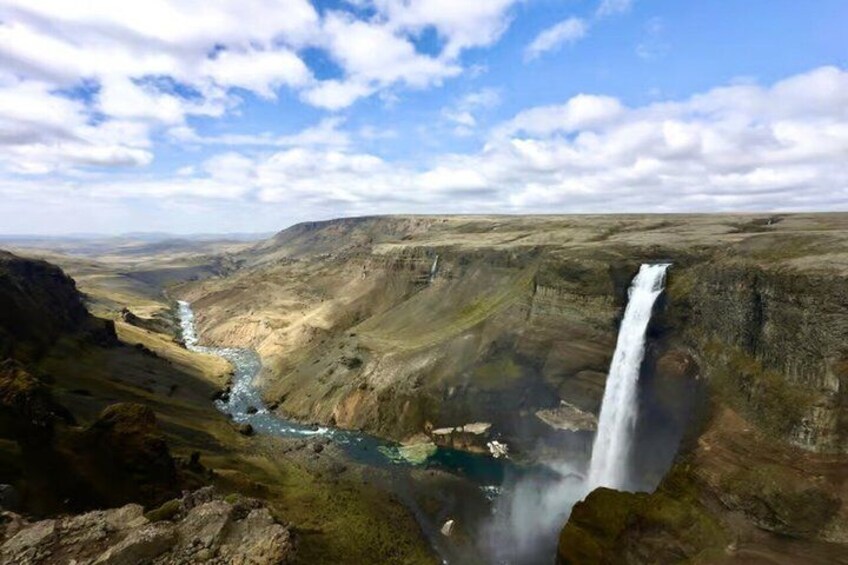 Ein Wasserfall stürzt eine steile Klippe hinab, umgeben von einer kargen Landschaft mit einem Fluss, der durch ein Tal fließt. 2