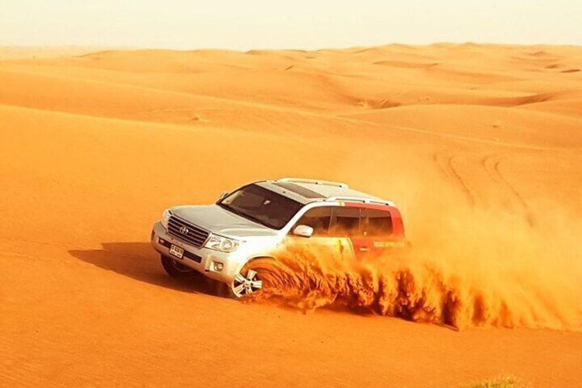 A white SUV driving through a desert with sand being kicked up behind it. 2