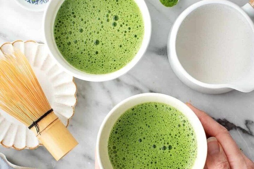 Twee kopjes groene thee, een garde en een glas water op een marmeren oppervlak. 5