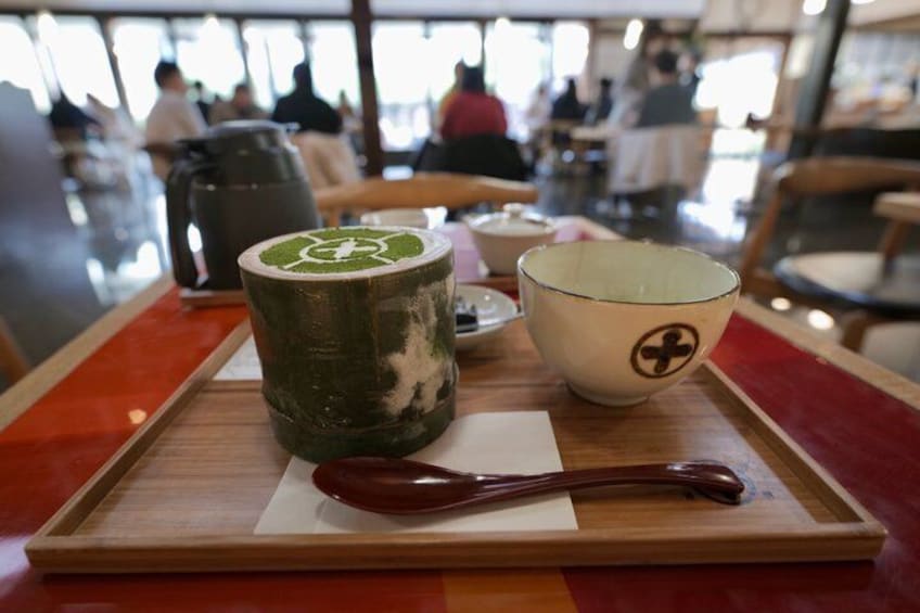 Een dienblad met een groene mok, een witte kom met een zwart symbool, en een houten lepel op een tafel in een café. 4