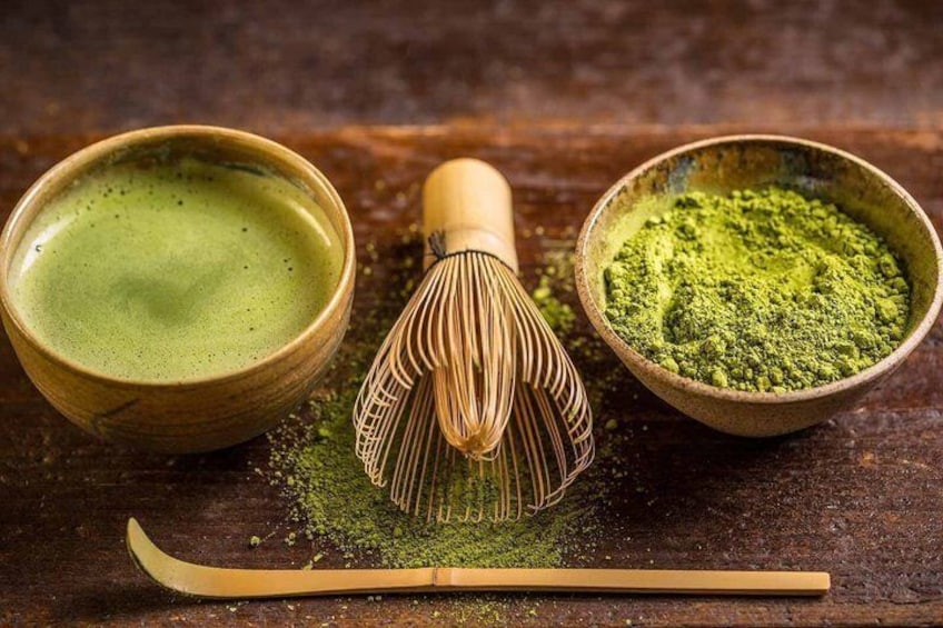 Een houten garde, twee kommen matcha en een bamboe lepel op een houten ondergrond. 1