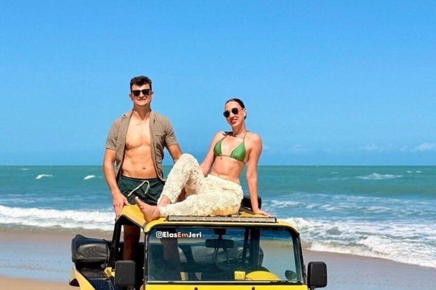 A beach scene with a yellow vehicle and two people standing on it. 2