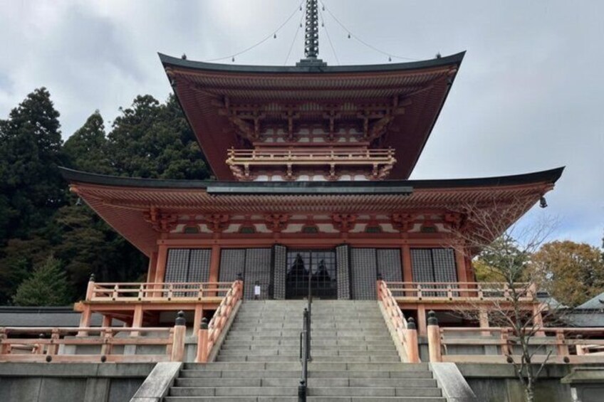 A traditional Japanese pagoda with a multi-tiered roof, a stone staircase leading up to it, and a backdrop of trees. 2