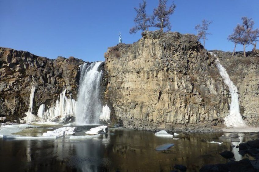 A waterfall cascading into a pool surrounded by rocky cliffs and sparse trees. 1