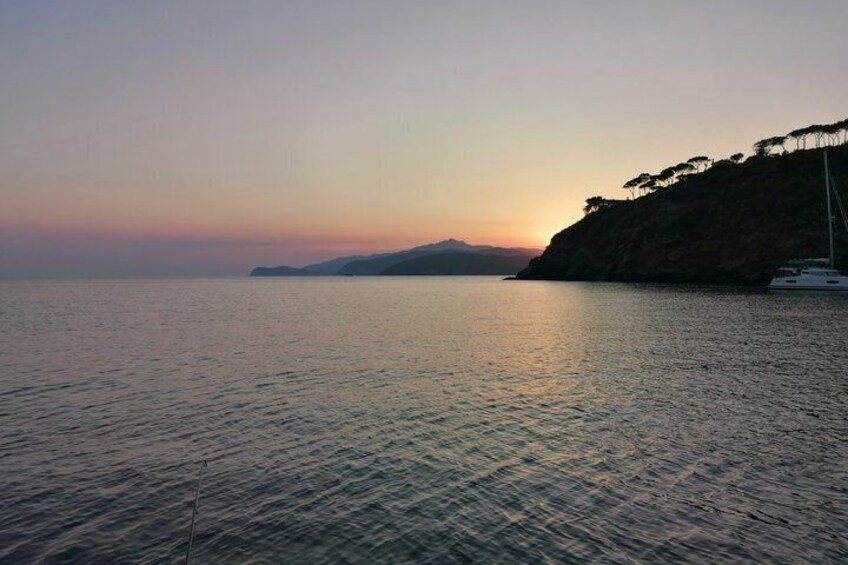 A calm sea at sunset with a boat on the right and a mountain in the background. 4