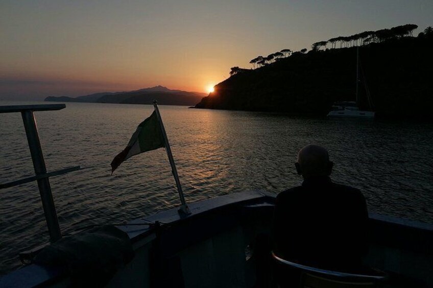 A sunset over a body of water with a flag and a sailboat in the distance. 1