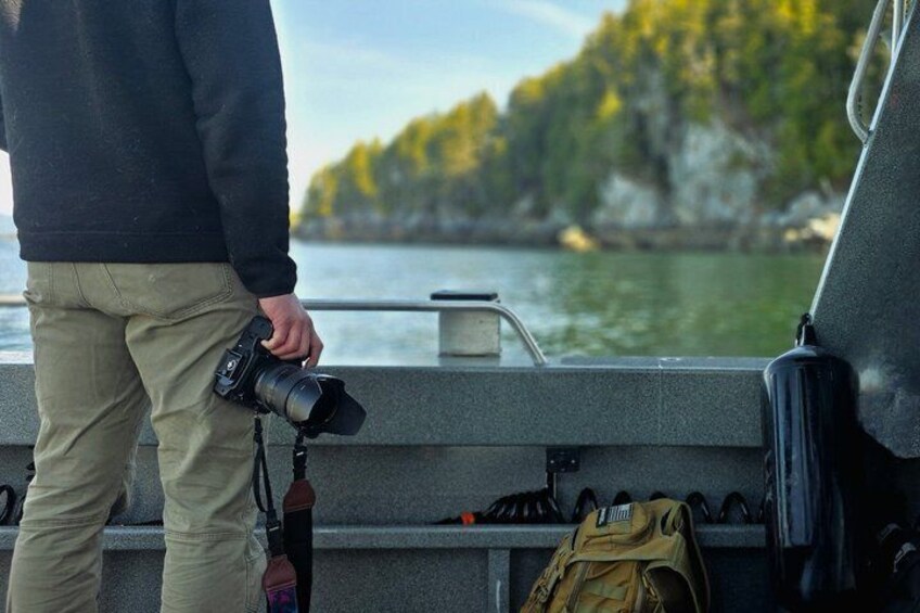 Een persoon houdt een camera vast op een boot, met een bebost oeverlandschap op de achtergrond. 4