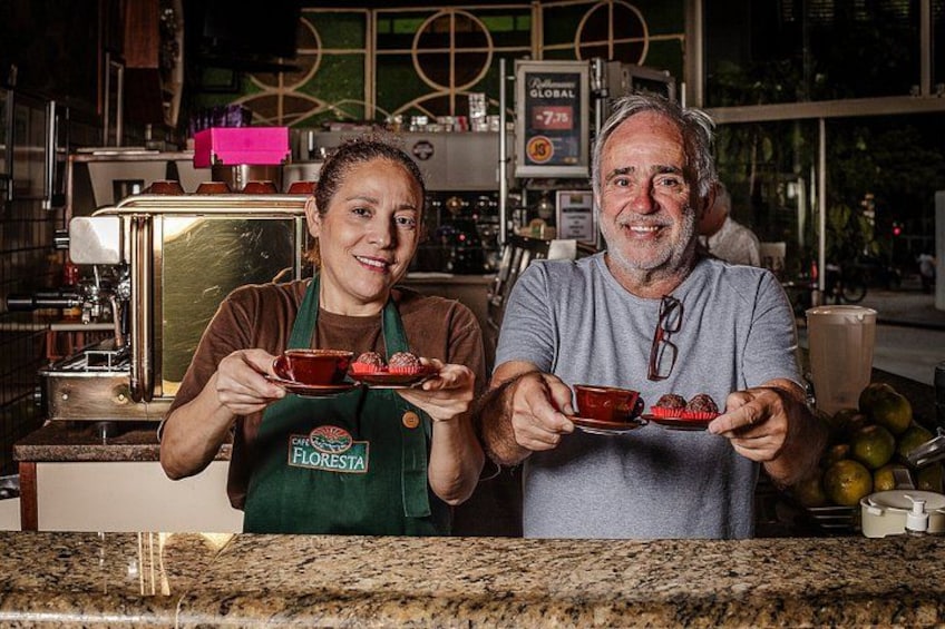 Two people holding cups of coffee in a cafe with a coffee machine and a sign in the background. 3